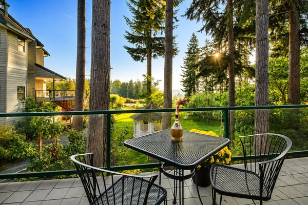 Hot tub with bubbling water on a sunny deck surrounded by tall evergreen trees and wooden house with red railing