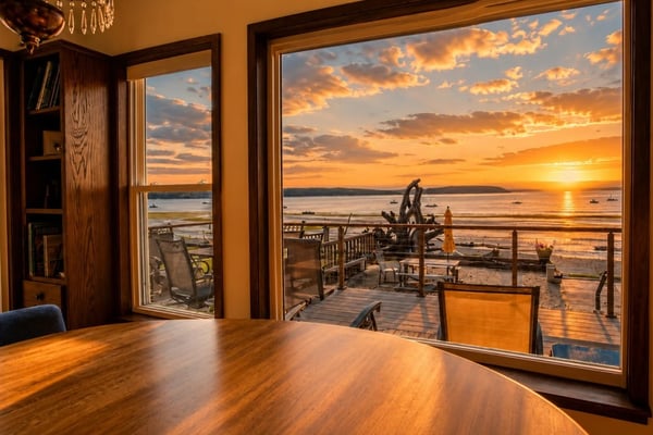 Modern waterfront home with expansive deck, Adirondack chairs, fire pit, and bay views at sunset