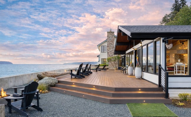 Modern open-plan living space with dining table, blue sofa, spiral staircase, and ocean views through large windows